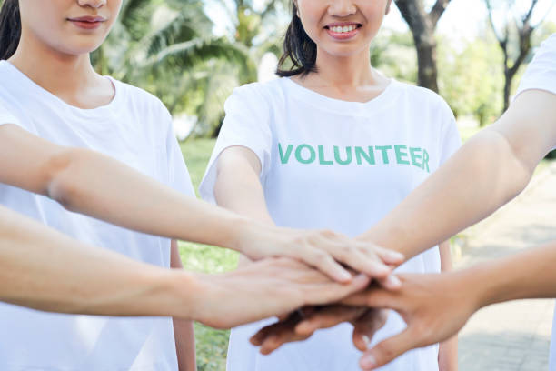 Close-up of young volunteers standing in a circle and holding hands together outdoors in summer day