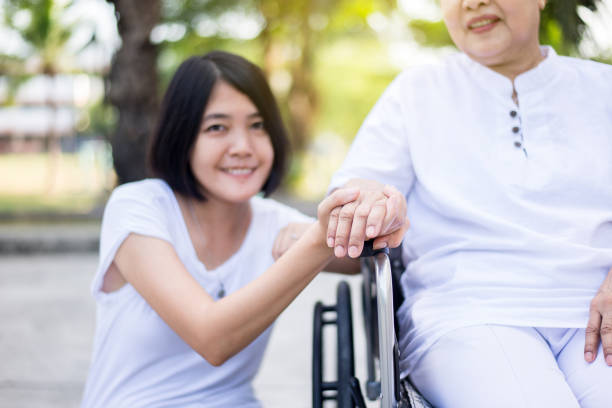 Caregiver hands holding to asian elderly woman sitting on wheelchair at outdoor,Take care and support,Senior insurance concept
